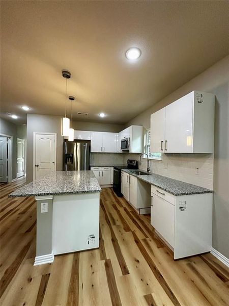 Kitchen featuring appliances with stainless steel finishes, light hardwood / wood-style flooring, decorative light fixtures, a kitchen island, and white cabinetry