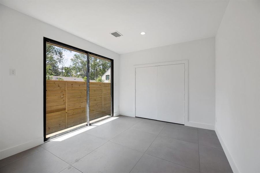 This is a bright, modern room with large sliding glass doors leading to a fenced outdoor area, providing ample natural light. The space features clean lines, a neutral color palette, and  perfect for customizing to your taste. A built-in closet offers convenient storage