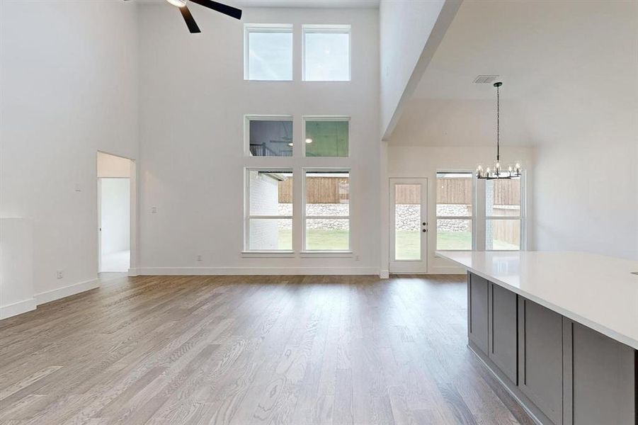 Unfurnished living room featuring ceiling fan with notable chandelier, hardwood / wood-style flooring, and a towering ceiling