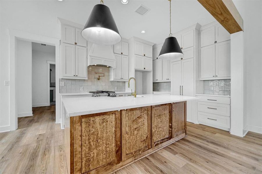 Kitchen featuring a center island with sink, backsplash, and light wood-type flooring