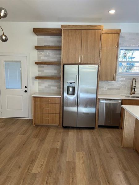 Kitchen with stainless steel appliances, sink, light hardwood / wood-style flooring, and backsplash