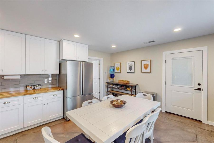 Kitchen with wooden counters, white cabinets, tasteful backsplash, and stainless steel refrigerator