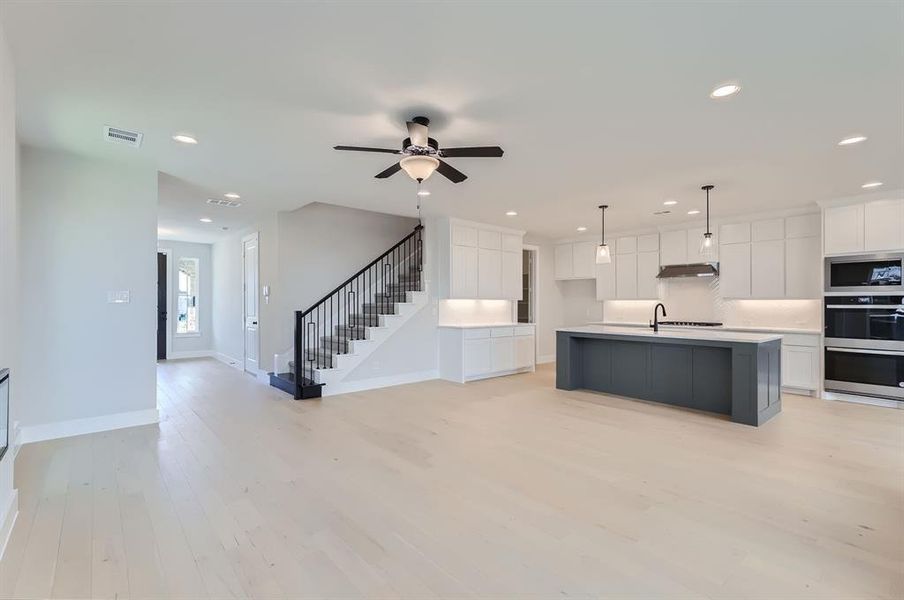 Kitchen with light hardwood / wood-style flooring, stainless steel appliances, a center island with sink, pendant lighting, and white cabinets