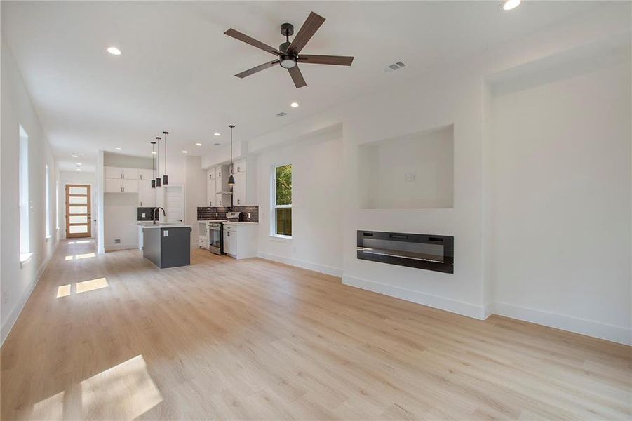 Unfurnished living room featuring light wood-type flooring, ceiling fan, and sink