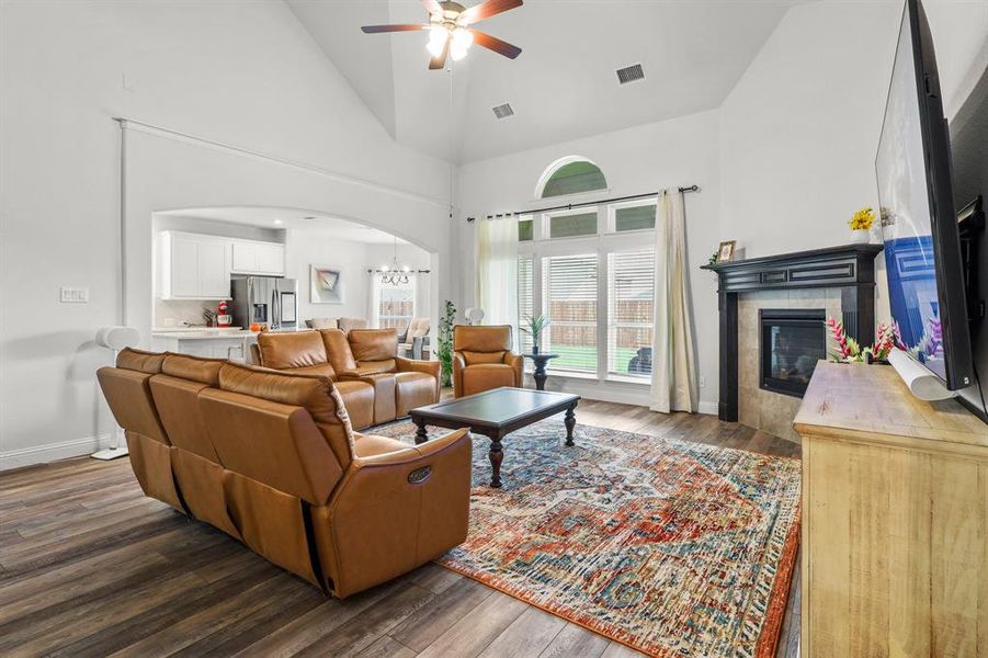 Living room with ceiling fan with notable chandelier, dark hardwood / wood-style floors, a fireplace, and high vaulted ceiling