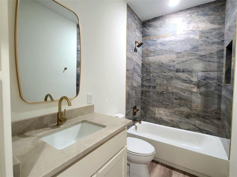 Full bathroom featuring vanity, toilet, tiled shower / bath combo, and hardwood / wood-style flooring