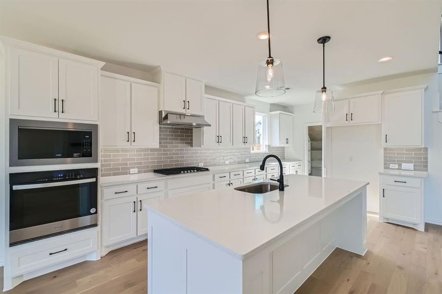 Kitchen featuring decorative backsplash, stainless steel appliances, a center island with sink, sink, and white cabinets