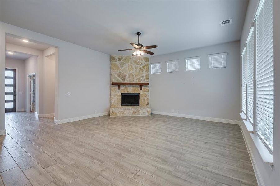 Unfurnished living room featuring a stone fireplace, light wood-type flooring, and ceiling fan