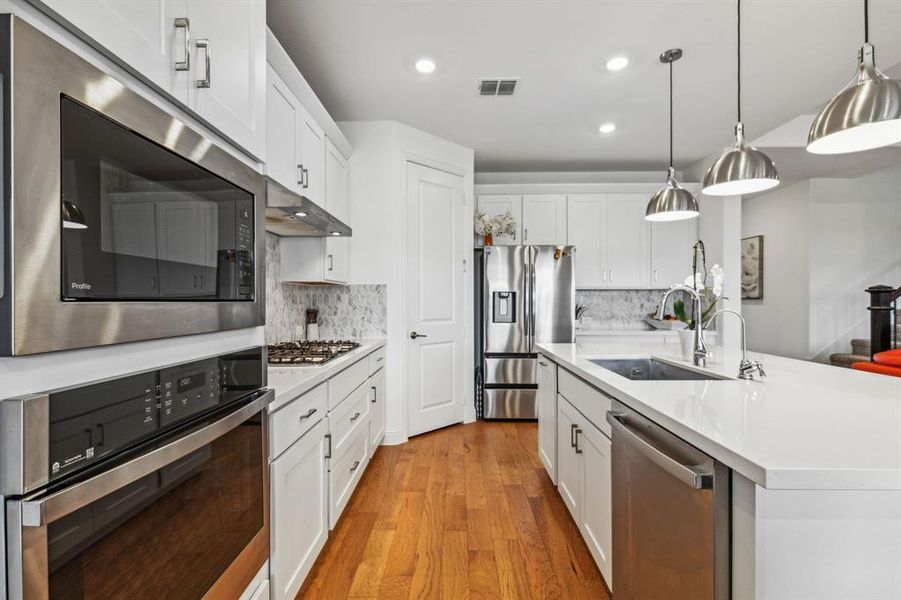 Kitchen with decorative light fixtures, tasteful backsplash, stainless steel appliances, and light hardwood floors