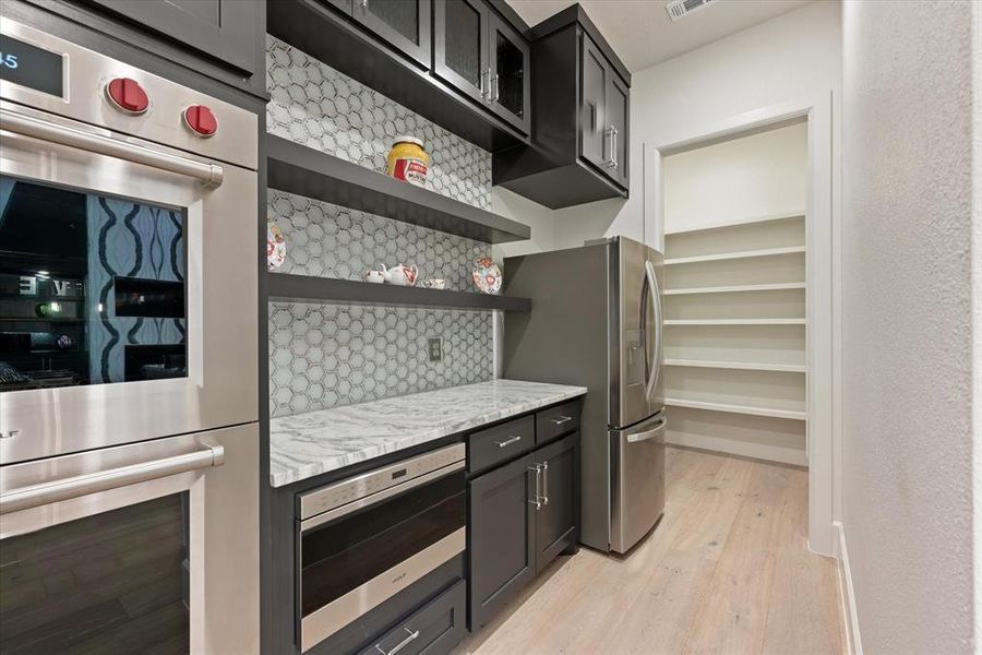 Kitchen with stainless steel appliances, light stone countertops, tasteful backsplash, and light hardwood / wood-style floors