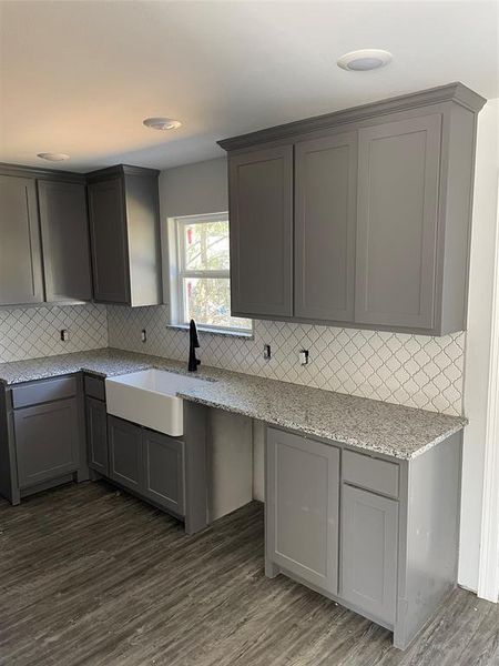 Kitchen featuring dark wood-type flooring, light stone counters, decorative backsplash, and sink