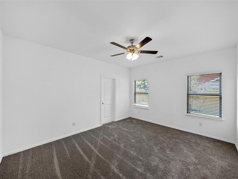 Unfurnished room featuring dark colored carpet, a healthy amount of sunlight, and ceiling fan