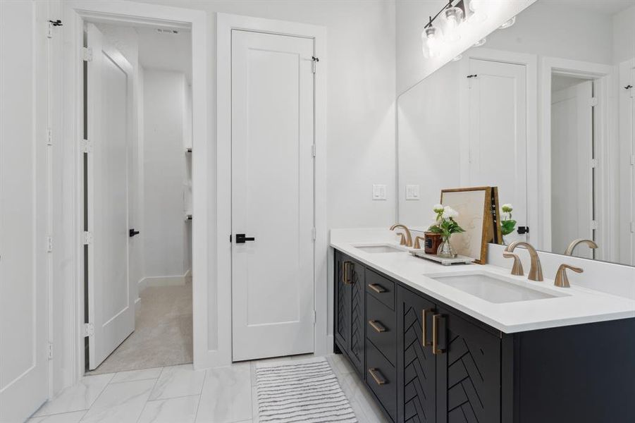 This bathroom features a sleek, dual-sink vanity with stylish black cabinetry, accented by brass fixtures and a large, well-lit mirror, creating a luxurious and contemporary feel.