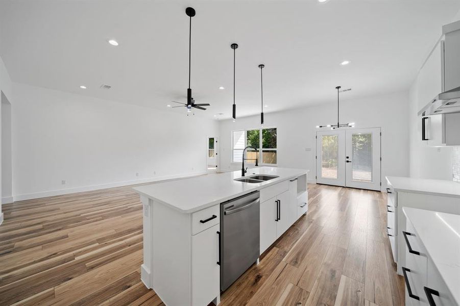 Kitchen featuring sink, dishwasher, white cabinetry, light hardwood / wood-style floors, and a center island with sink