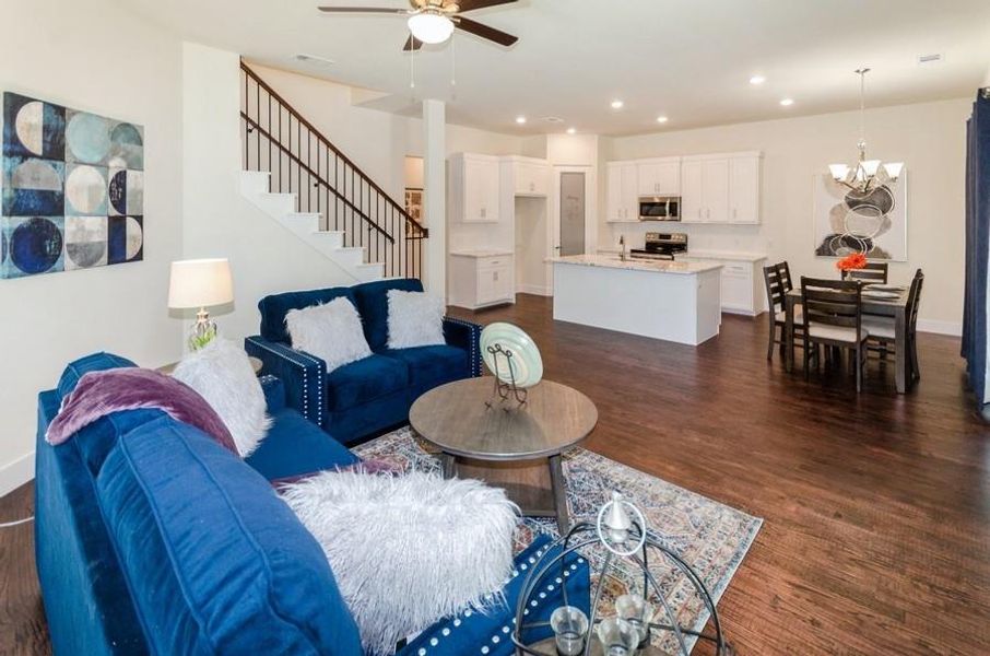 Living room with ceiling fan with notable chandelier and dark hardwood / wood-style flooring