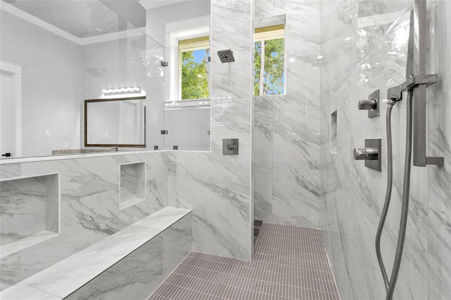 Expansive wall-through shower is loaded with frameless glass, inset storage, delta hardware, a shower bench that runs the length of the shower & rain, wall and handheld shower heads.