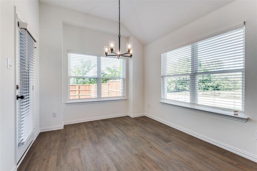 Empty room featuring vaulted ceiling, a notable chandelier, and dark hardwood / wood-style flooring