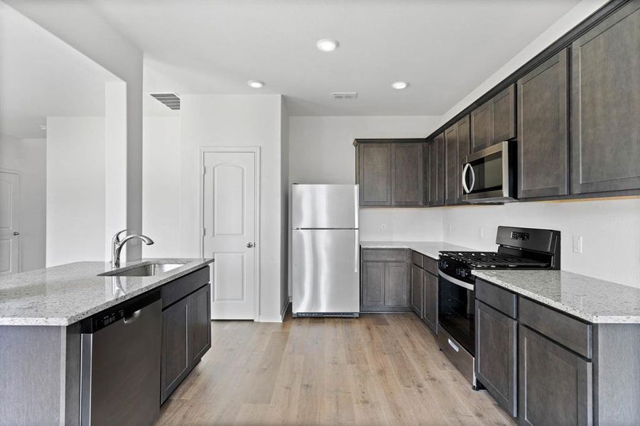 Kitchen featuring appliances with stainless steel finishes, light stone countertops, light wood-style floors, sink, and dark cabinets