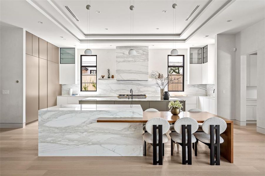 The oversized breakfast table and serving bar were custom created for this home and are adorned with a chic, wooden surface and a higher marble countertop that elegantly cascades on all sides.