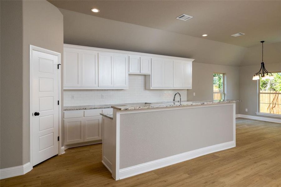 Kitchen featuring white cabinetry, light hardwood / wood-style floors, tasteful backsplash, and an island with sink