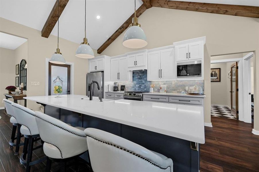 Kitchen featuring dark hardwood / wood-style floors, beam ceiling, decorative light fixtures, and a large island with sink