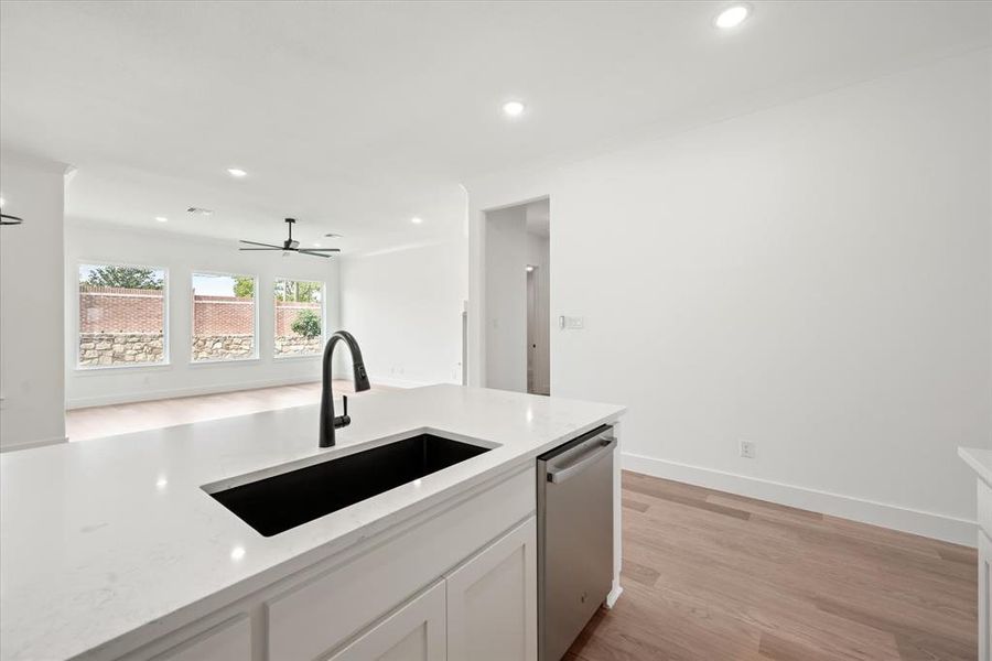 Kitchen featuring stainless steel dishwasher, ceiling fan, sink, light stone countertops, and light hardwood / wood-style flooring