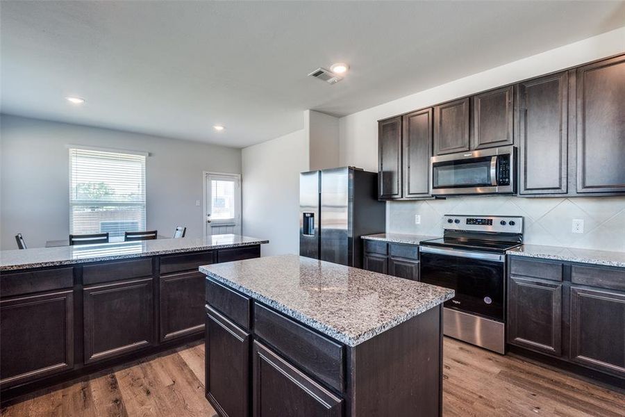 Kitchen featuring backsplash, stainless steel appliances, wood-type flooring, a center island, and dark brown cabinetry