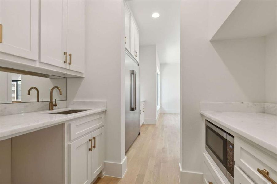 Kitchen featuring white cabinets, sink, light hardwood / wood-style flooring, light stone countertops, and stainless steel microwave