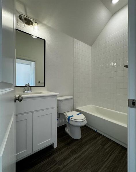 Full bathroom featuring hardwood / wood-style flooring, lofted ceiling, bathing tub / shower combination, vanity, and toilet