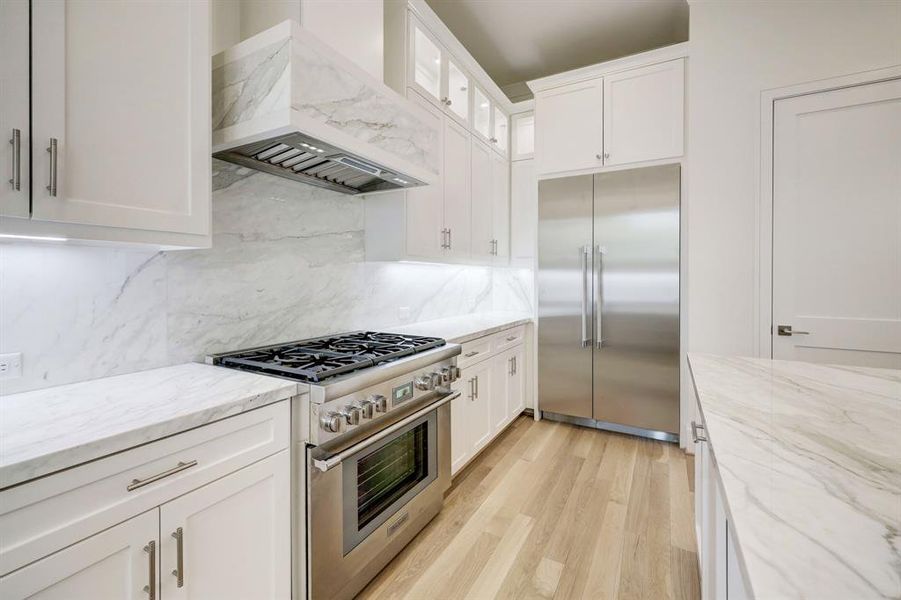 Kitchen features Thermador stainless appliances including this 6 burner gas range that is surrounded by marble countertops and backsplash. Notice the detail on the vent hood!