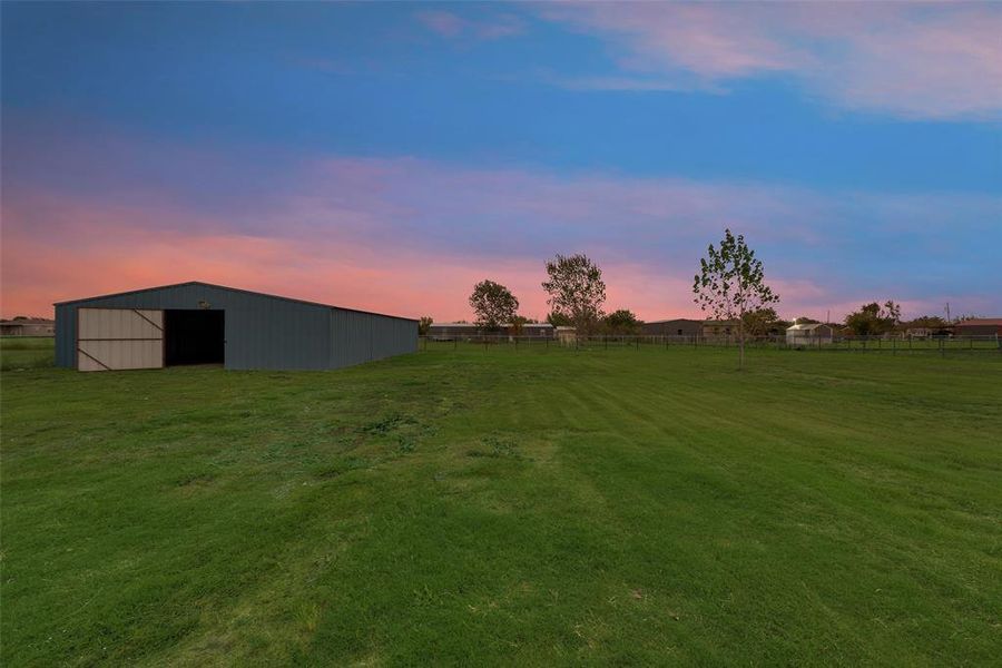 Yard at dusk featuring an outbuilding and a rural view