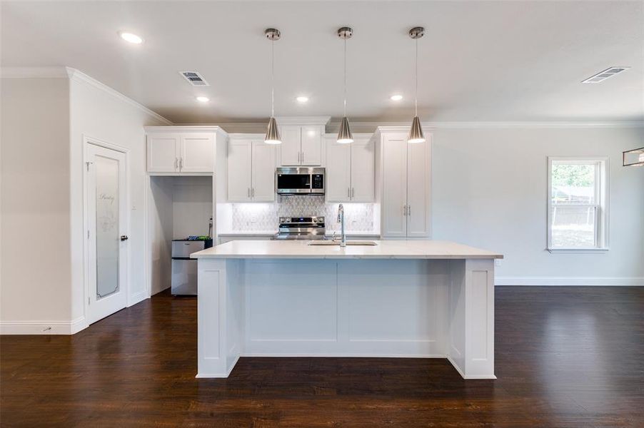 Kitchen featuring white cabinets, dark hardwood / wood-style floors, appliances with stainless steel finishes, decorative backsplash, and a center island with sink