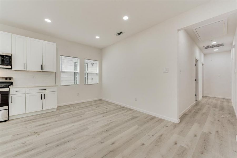 Kitchen featuring appliances with stainless steel finishes, light wood-type flooring, white cabinetry, and decorative backsplash