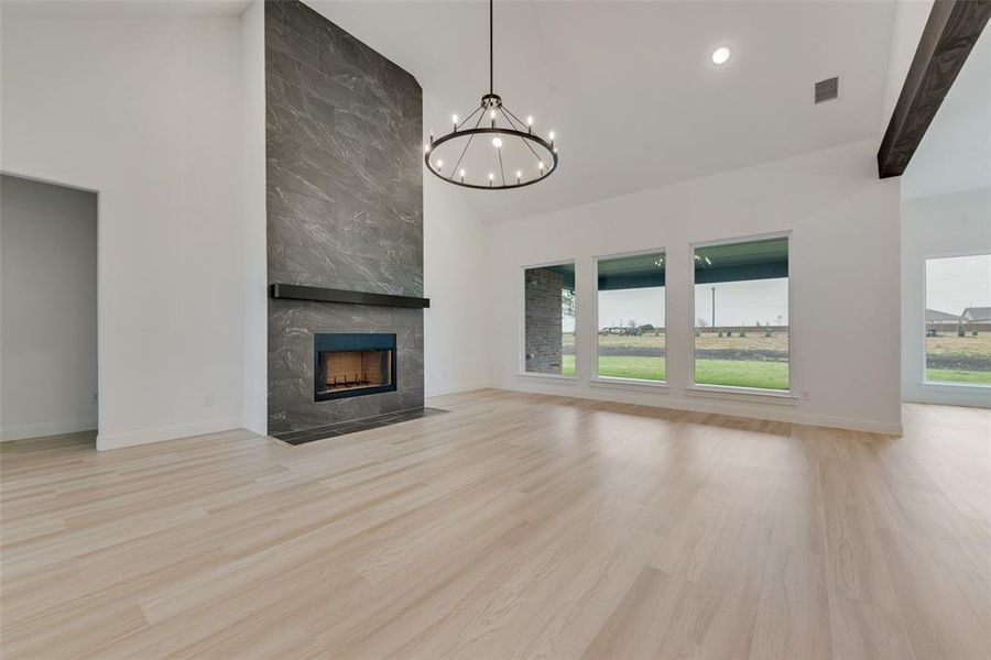 Unfurnished living room with light wood-type flooring, a tile fireplace, an inviting chandelier, and beamed ceiling