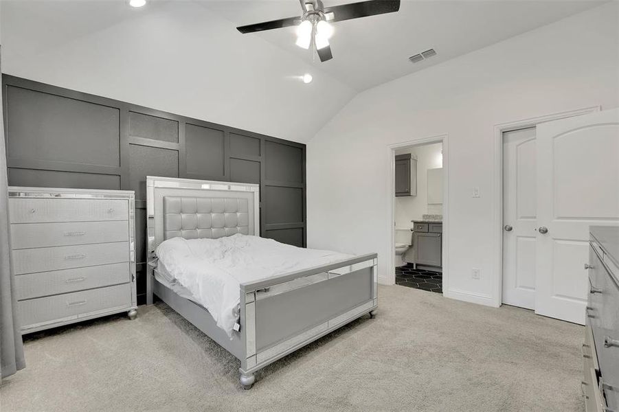 Carpeted bedroom with ensuite bathroom, ceiling fan, and vaulted ceiling