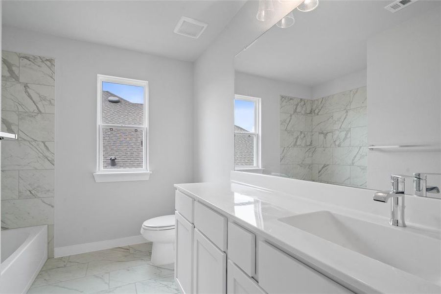 Secondary bath features tile flooring, bath/shower combo with tile surround, stained wood cabinets, beautiful light countertops, mirror, dark, sleek fixtures and modern finishes!