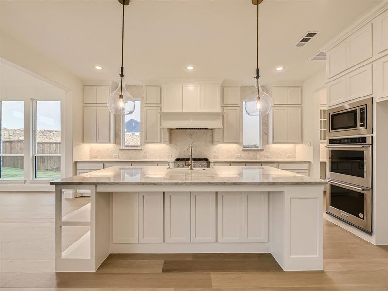 Kitchen featuring appliances with stainless steel finishes, light hardwood / wood-style flooring, pendant lighting, and a kitchen island with sink