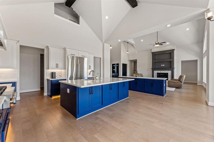 Kitchen featuring white cabinets, high vaulted ceiling, a center island with sink, ceiling fan, and blue cabinetry