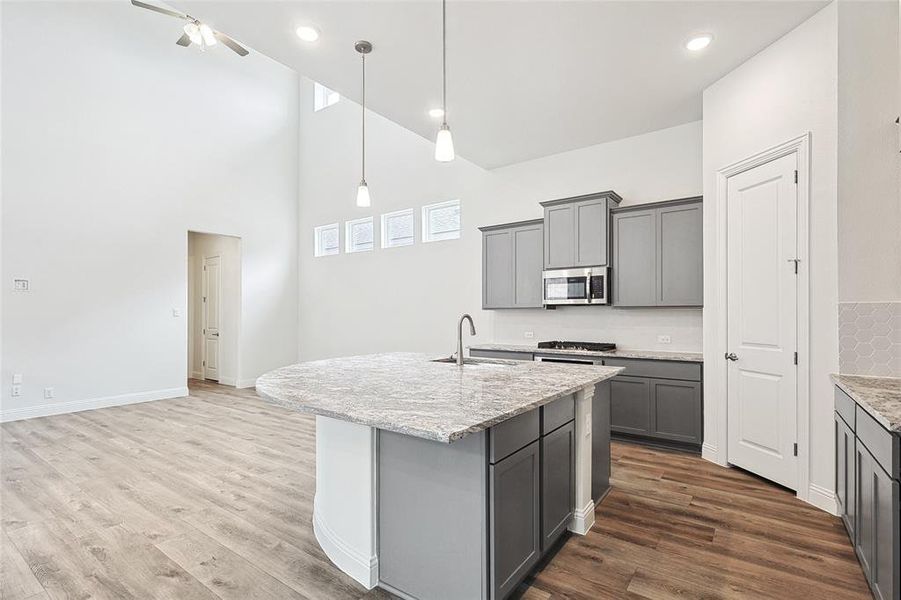 Kitchen with an island with sink, hanging light fixtures, gray cabinetry, hardwood / wood-style floors, and sink