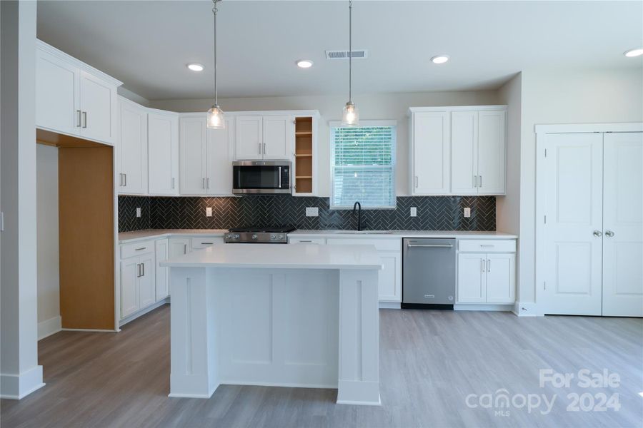Kitchen features upgraded cabinets, appliances and lighting. Kitchen also features a trimmed island and glossy herringbone patterned backsplash