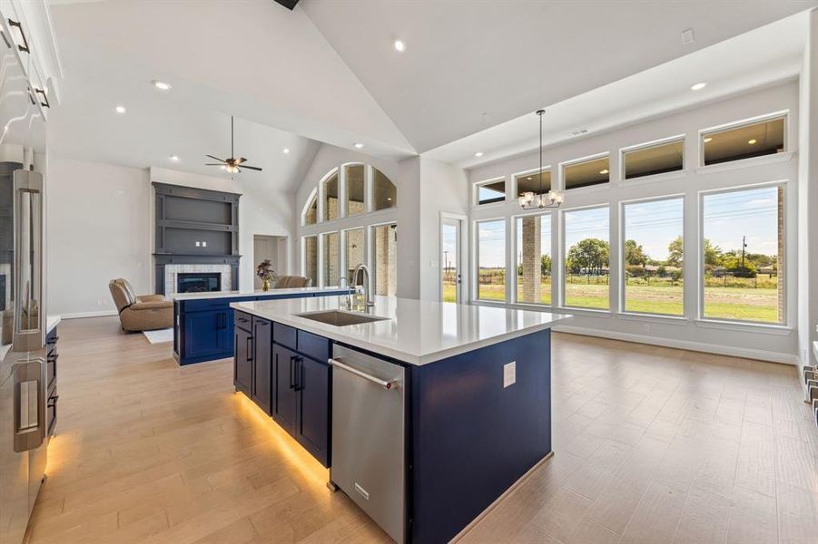 Kitchen featuring sink, a kitchen island with sink, light hardwood / wood-style flooring, high vaulted ceiling, and ceiling fan with notable chandelier