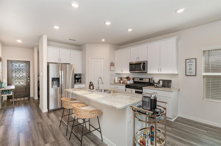 Kitchen with a breakfast bar, a kitchen island with sink, stainless steel appliances, and white cabinets