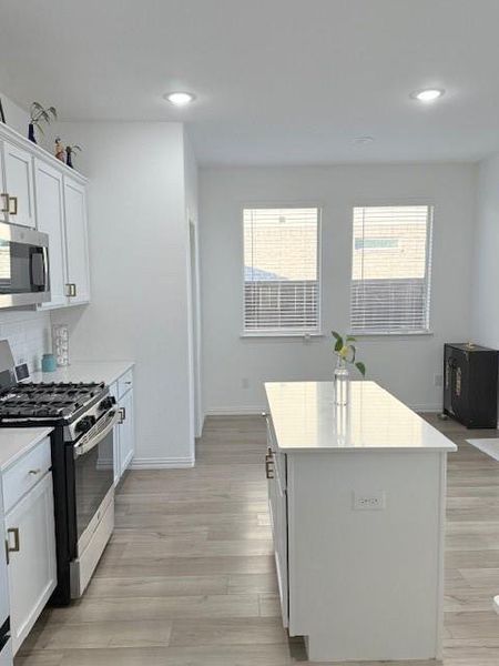 Kitchen with a kitchen island, white cabinetry, backsplash, range, and light hardwood / wood-style flooring