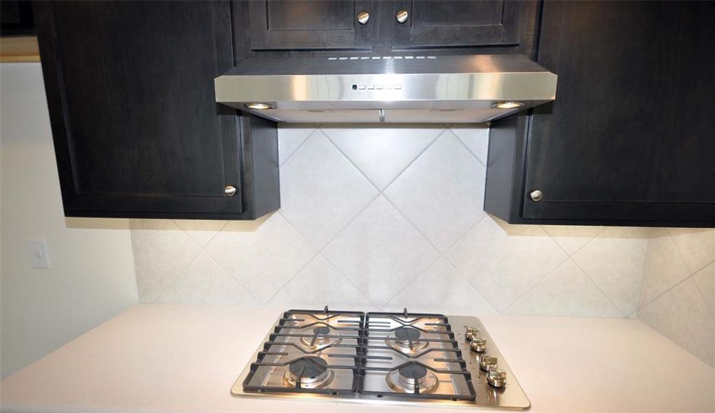 A gas cooktop under an externally vented hood, standard at Cervelle Homes.