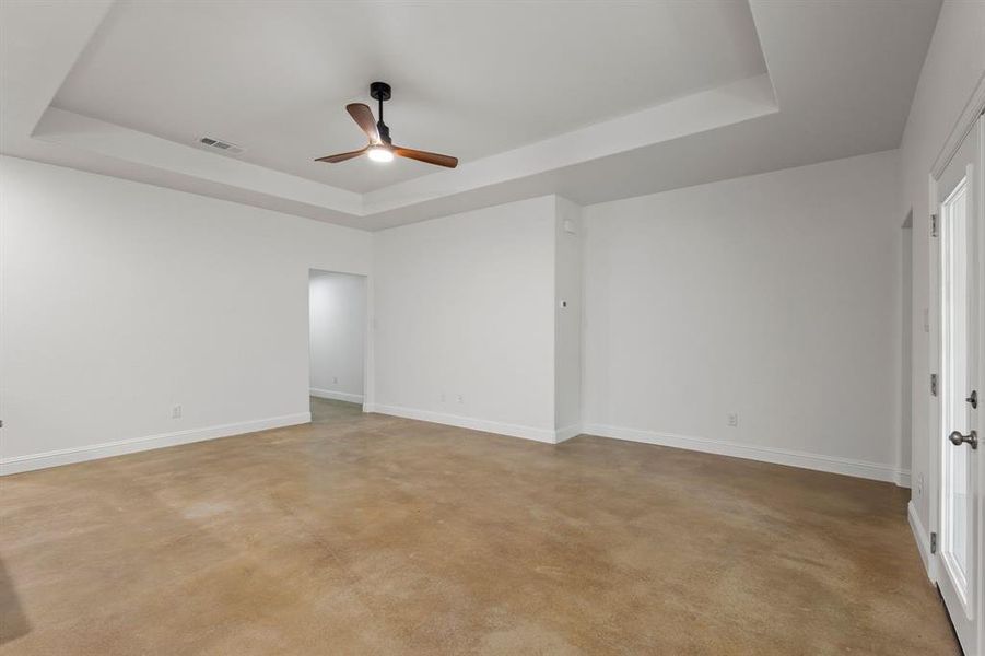 Empty room with a tray ceiling, light colored carpet, and ceiling fan