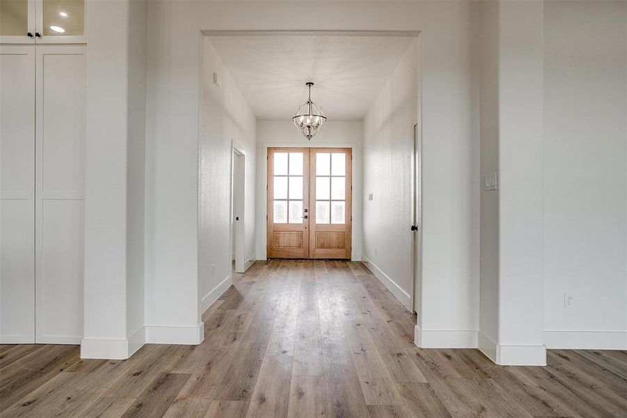 Doorway featuring light wood-type flooring, a chandelier, and french doors