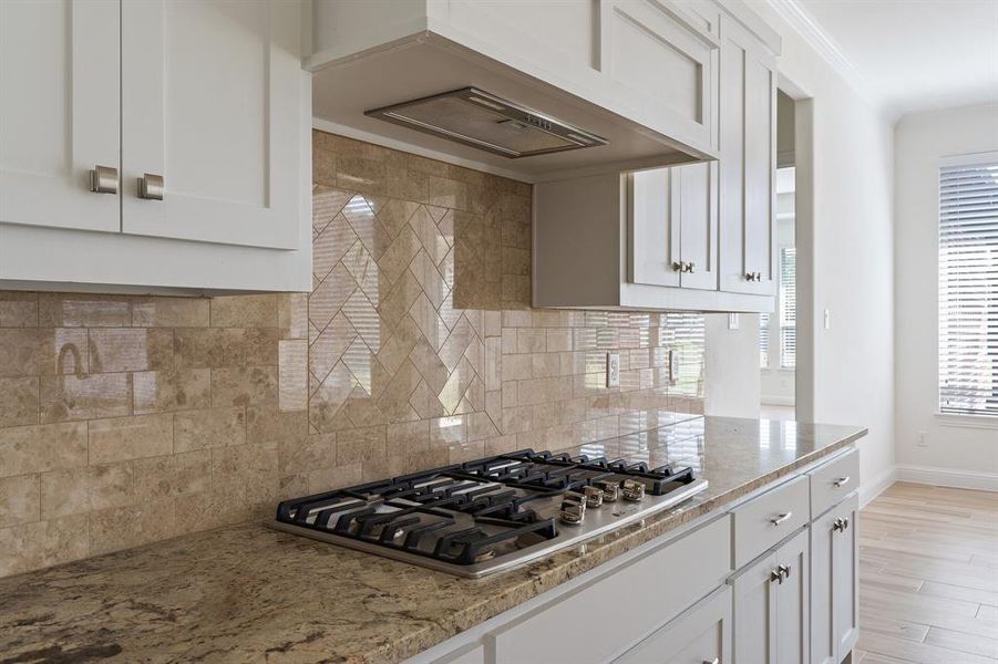 Kitchen featuring light hardwood / wood-style flooring, white cabinets, decorative backsplash, and stainless steel gas stovetop