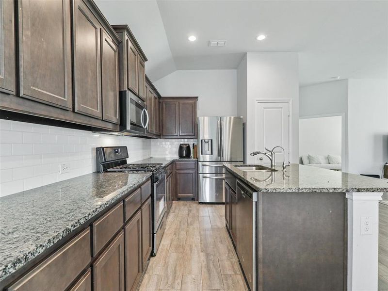 Kitchen featuring light / wood-style flooring, tasteful backsplash, a kitchen island with sink, appliances with stainless steel finishes, and sink