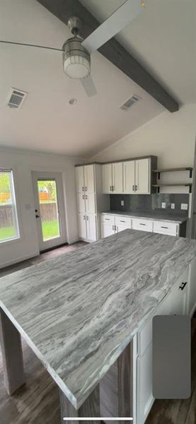 Kitchen with light stone countertops, ceiling fan, dark hardwood / wood-style floors, lofted ceiling with beams, and white cabinets