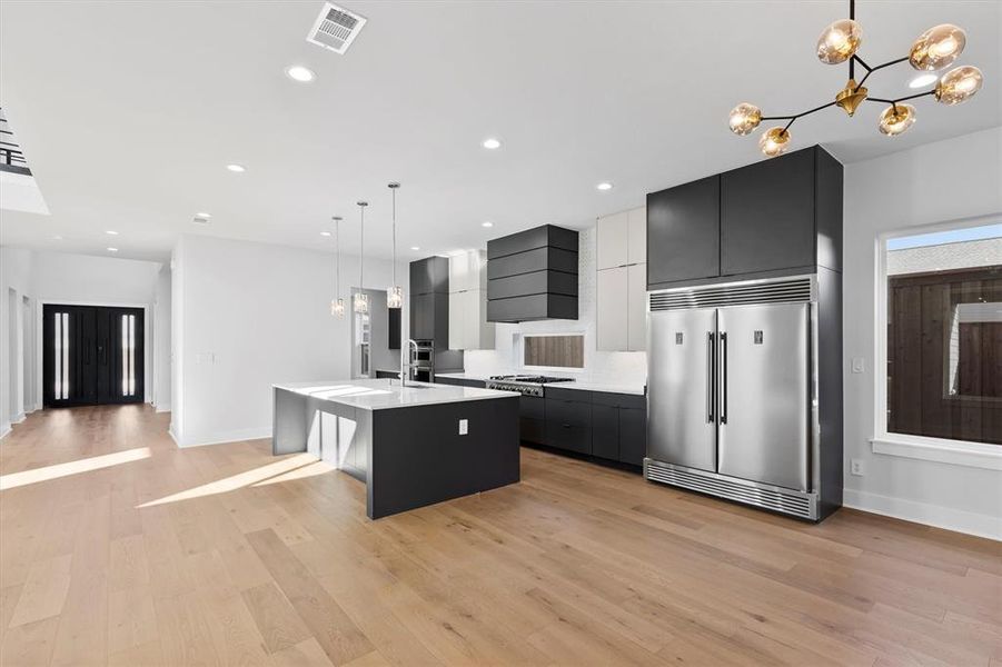 Kitchen with a center island with sink, decorative light fixtures, light wood-type flooring, and built in refrigerator